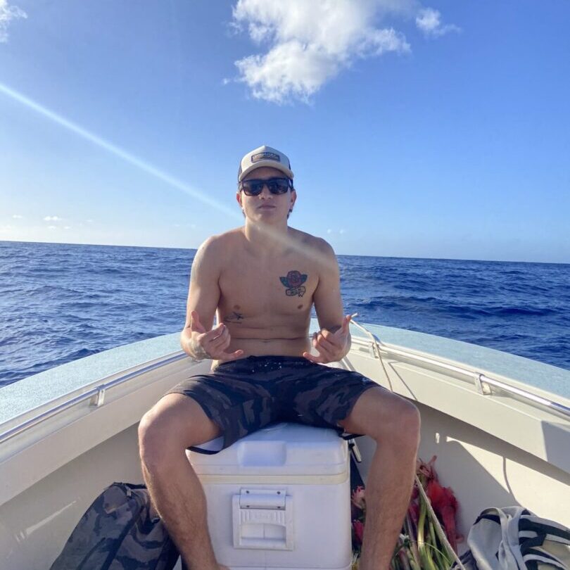 A man sitting on the back of a boat in the ocean.